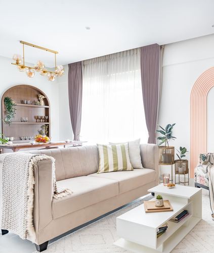 Beige tufted sofa with striped cushion in living room with arched wooden shelf and blush arch wall