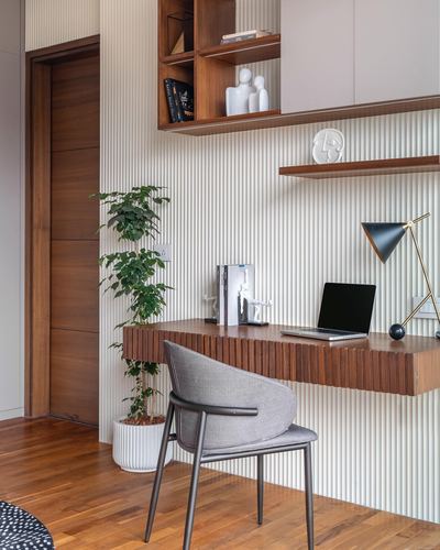 Floating wooden desk with laptop against fluted wall, grey chair, potted plant beside wooden door
