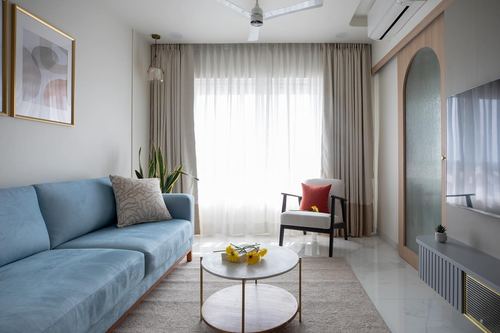 Living room with blue velvet sofa, sheer curtains, round marble coffee table and arched glass door