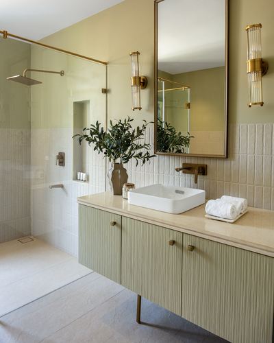 Sage green fluted vanity with vessel sink, brass fixtures, and walk-in shower in a bathroom