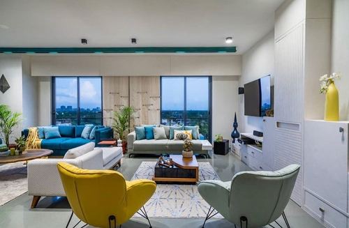 Contemporary living room with teal sofa, yellow and mint chairs, city skyline through glass windows at dusk