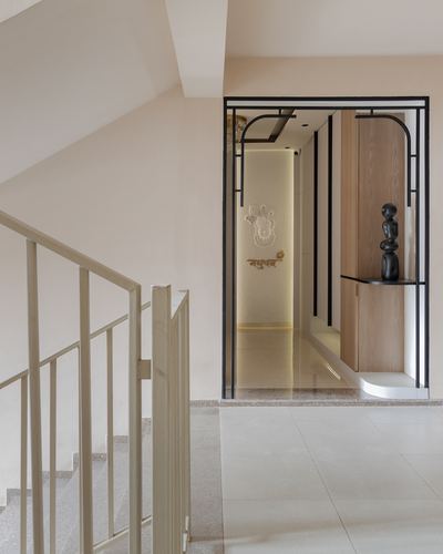 Staircase landing beside an arched black metal frame leading to a textured foyer with a wooden console and sculpture.