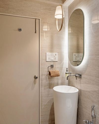 Beige stone powder room with backlit oval mirror, pendant light, and cylindrical pedestal basin