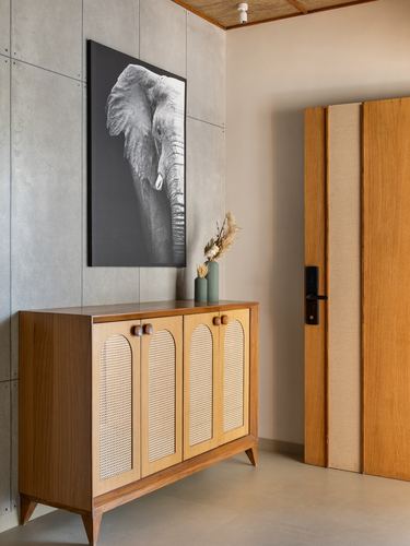 Wooden cane-front sideboard below a black and white elephant photograph in a stone-floored foyer.
