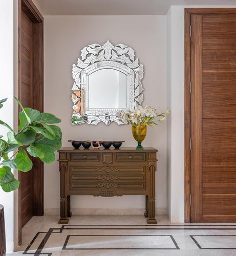 Entryway with carved wood console, venetian mirror, brass vase, and fiddle leaf fig plant