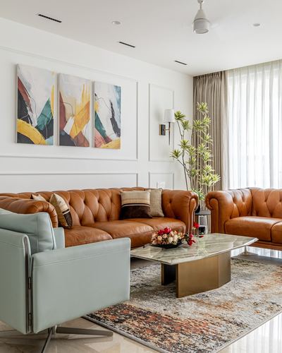 Living room with tan leather chesterfield sofas, sage armchair, and marble coffee table on patterned rug