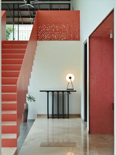 Red perforated steel staircase beside a mosaic-tiled doorway in a marble-floored foyer
