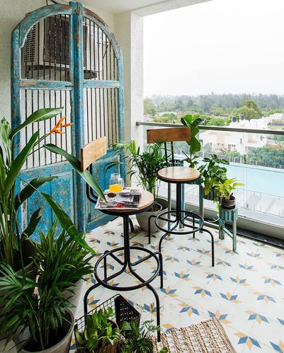 Balcony with patterned tile floor, black bar stools, plants, and a weathered blue arched wooden screen door