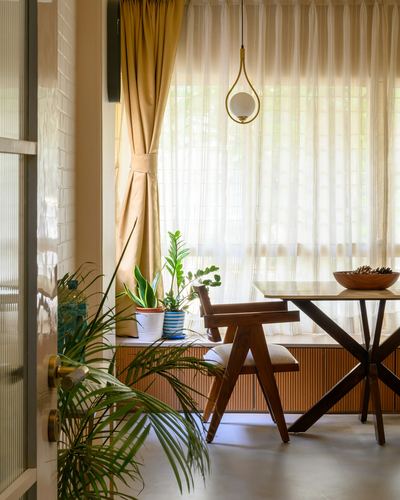 Sunlit dining nook with wooden chair, marble-top table, sheer curtains, and potted plants