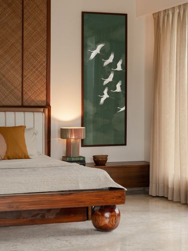 Bedroom corner with woven headboard panel, green crane artwork, and wood-and-marble floor