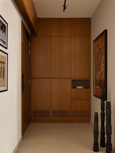 Entryway hallway with tall wood paneled storage wall, perforated lower panels, and framed art
