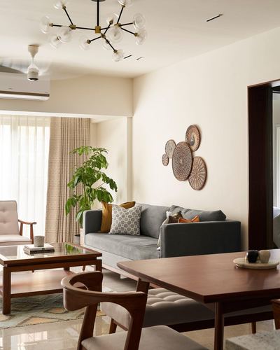 Living and dining area with grey sofa, wooden table, and circular wall art in Mumbai apartment
