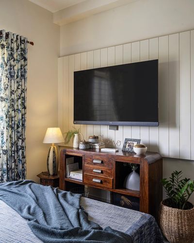 Bedroom with wooden sideboard, wall-mounted tv on paneled wall, floral curtain and blue bedspread