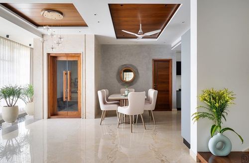 Neutral-toned dining area with round table, pink chairs, circular mirror, and wood ceiling coffer