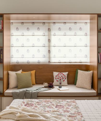 Wood-framed window seat with patterned roman blinds, cushions, throw, and small tray of grapes and coffee
