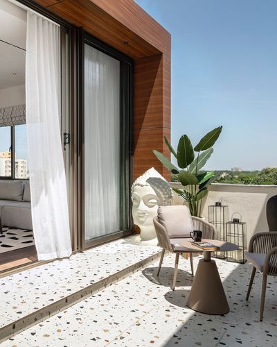 Terrazzo balcony with rattan chairs, buddha sculpture, and wood-clad sliding door under blue sky