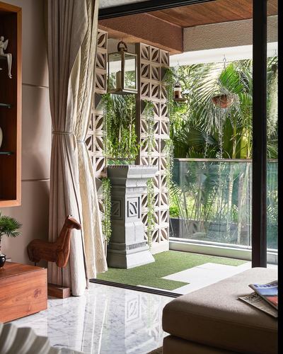 Living room opening through jaali screen to a plant-filled balcony with stone pedestal and lantern