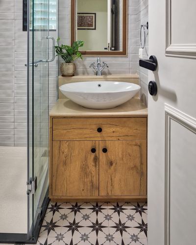 Bathroom vanity with wood cabinet, vessel sink, patterned floor tile, and glass shower door
