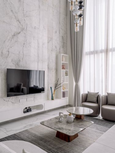 Double-height living room with marble wall, wall-mounted tv, and layered coffee tables