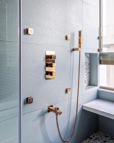 Fluted pale blue tile shower wall with copper fixtures and terrazzo niche