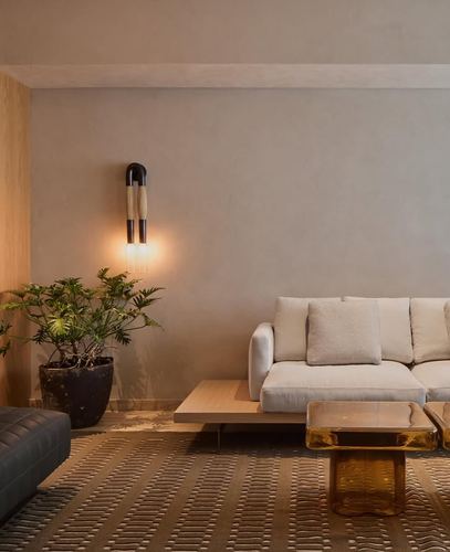 Minimalist living room with beige sofa, low wood table, amber glass table, and sculptural wall sconce beside a plant