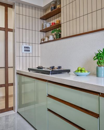Mumbai apartment kitchen with sage green glossy cabinets, terrazzo counter, and tiled backsplash with open wood shelves
