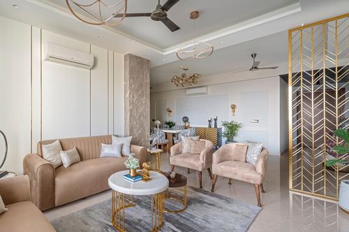 Beige living room with velvet sofa, round marble coffee tables, and brass jali screen divider