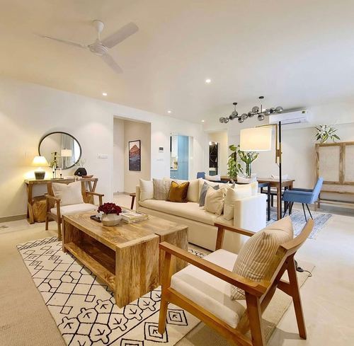 Open living room with cream sofa, wooden armchairs, round mirror, and dining area beyond