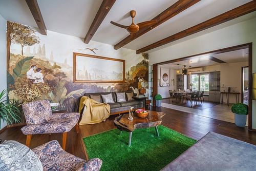 Living room with painted mural wall, exposed wood beams, cane armchair and green rug over dark wood floor