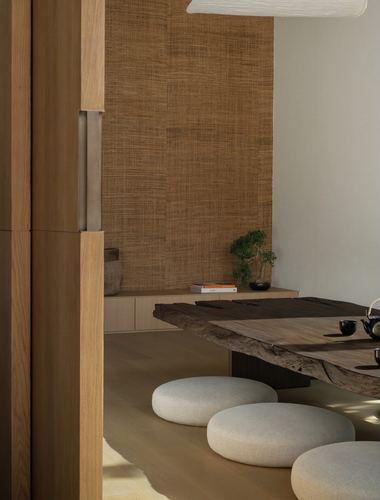 Low live-edge wood dining table with floor cushions against a woven textured wall