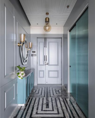 Grey entryway foyer with teal cabinet, round mirror, exposed bulb pendant, and geometric marble floor leading to a panelled door