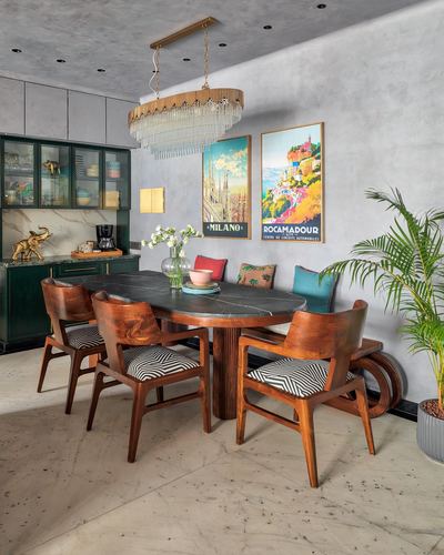 Dining room with marble oval table, wooden chairs, crystal chandelier and colorful travel posters on grey wall