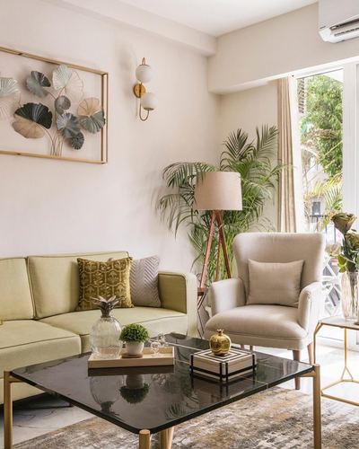 Living room corner with olive sofa, beige armchair, black marble table and leafy wall art