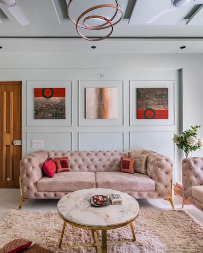 Blush chesterfield sofa facing round marble coffee table beneath framed art on paneled wall