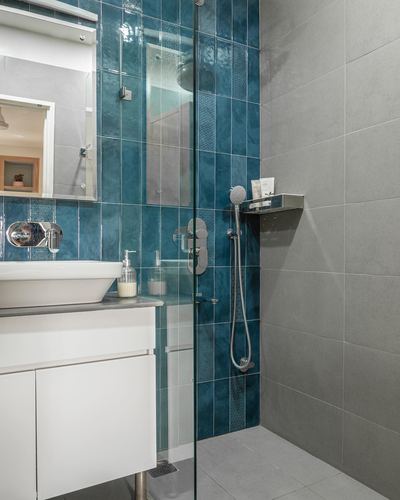 Bathroom with teal ribbed tile shower wall, glass partition, grey tile flooring and white vessel sink