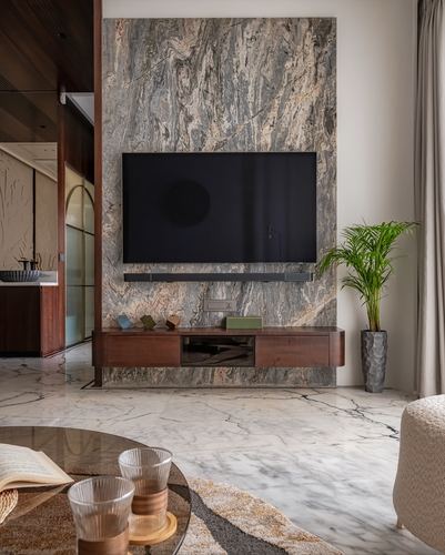 Living room with veined stone tv wall, floating wood console, marble floor and potted palm