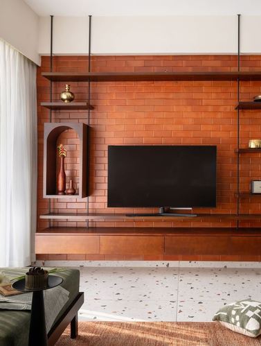 Terracotta brick tv wall with suspended wooden shelves, arched niche, terrazzo floor, and green bench.