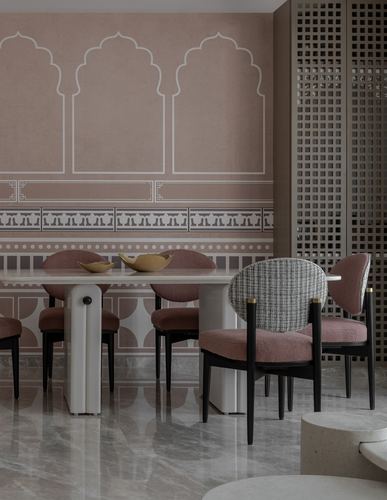 Dining table with pink chairs against a pink arched mural wall and jali screen