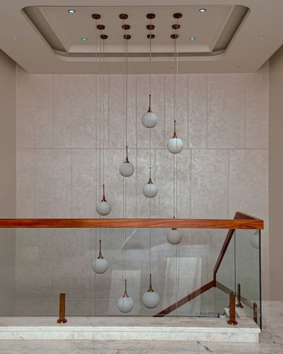 Cluster of globe pendant lights hanging over a marble staircase with glass and wood railing