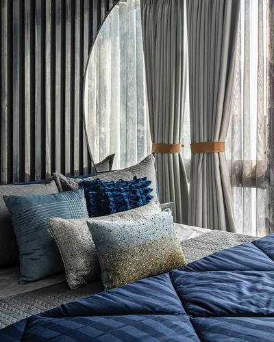 Bed with navy and silver cushions, round mirror, and sheer curtains with leather tiebacks