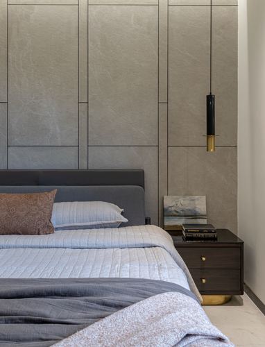 Bedroom corner with stone paneled wall, pendant light, dark wood nightstand and grey upholstered headboard