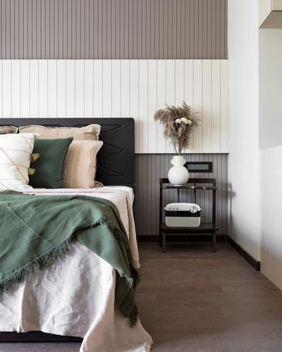 Bedroom with dark carved headboard, green and beige linens, ribbed paneled wall, and a nightstand with a white vase.