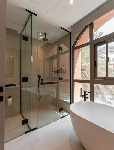 Bathroom with glass shower, freestanding tub, and arched window overlooking palm trees