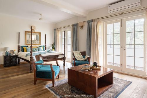Bedroom with carved wooden four-poster bed, teal velvet chairs, wooden coffee table and french doors to balcony