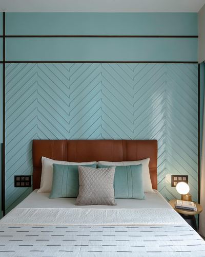 Bed with terracotta leather headboard against teal chevron-paneled wall in Mumbai bedroom