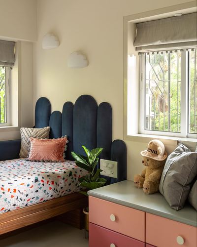 Child's bedroom with scalloped navy headboard, terrazzo-print bedding, pink dresser and teddy bear by window
