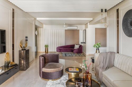 Living room with plum velvet curved sofa, brass tables, and marble flooring under a paneled ceiling