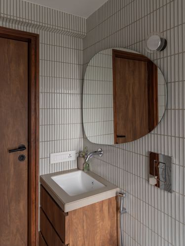 Bathroom vanity with organic mirror, ribbed tile walls, and wooden cabinetry beside a wooden door