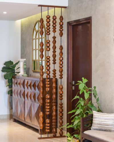 Turned wooden bead strands hang as a room divider beside an arched mirror and geometric sideboard in a foyer.