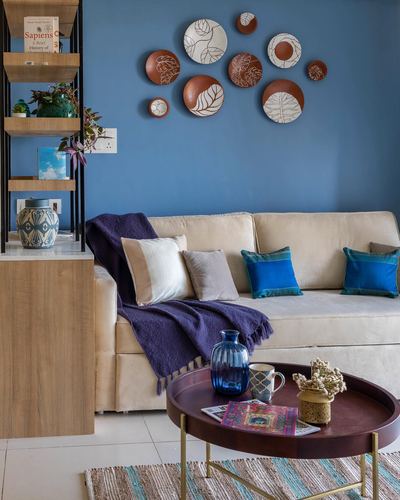 Blue living room wall with ceramic plates above a cream sofa and round wood coffee table